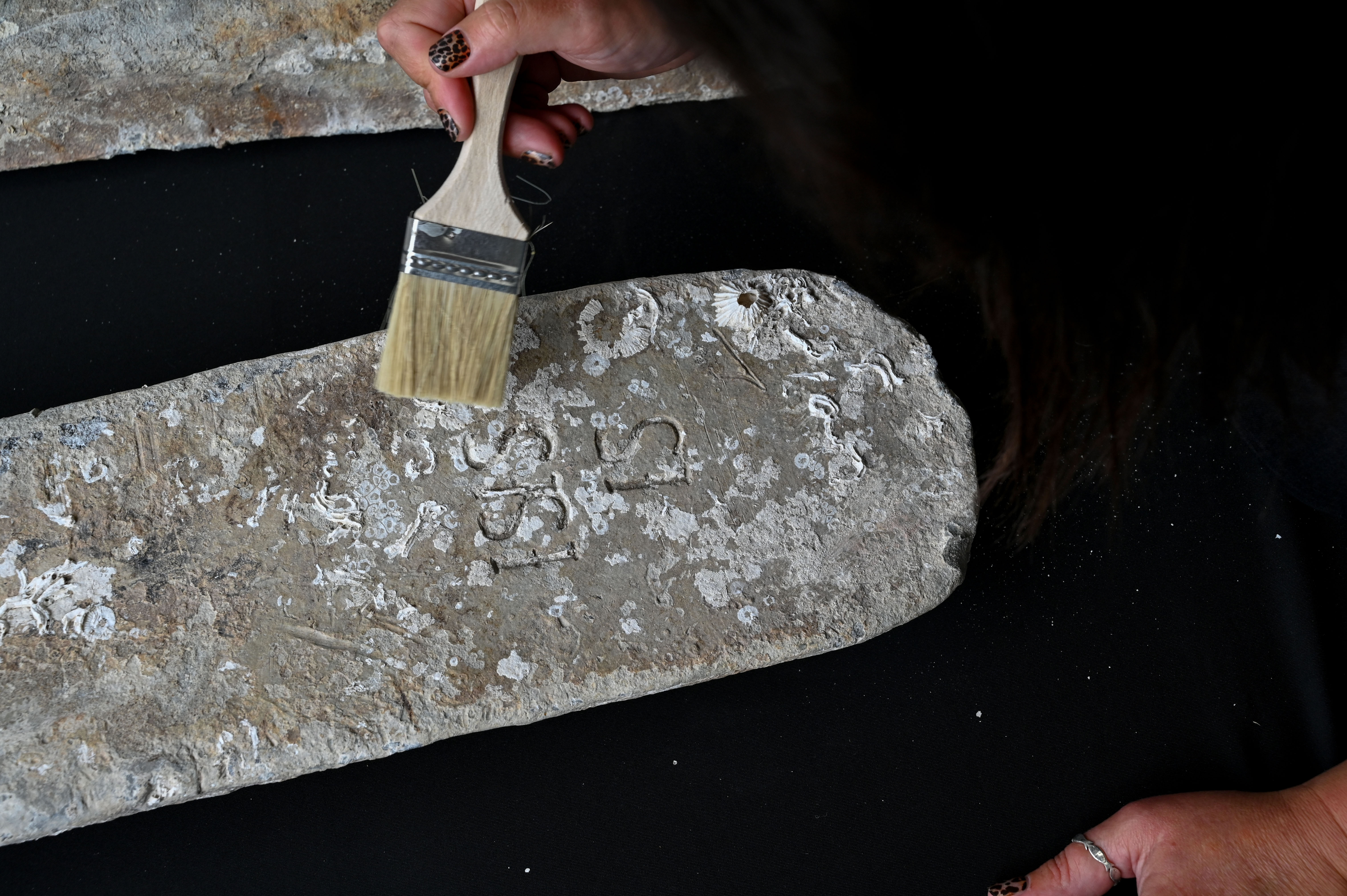 A hand holds a brush above markings on a lead ingot 