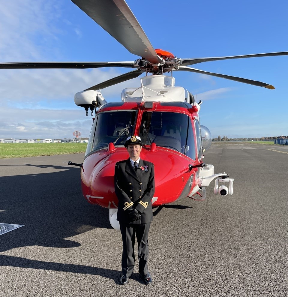 Female Coastguard in full dress uniform stood in front of red and white Coastguard helicopter