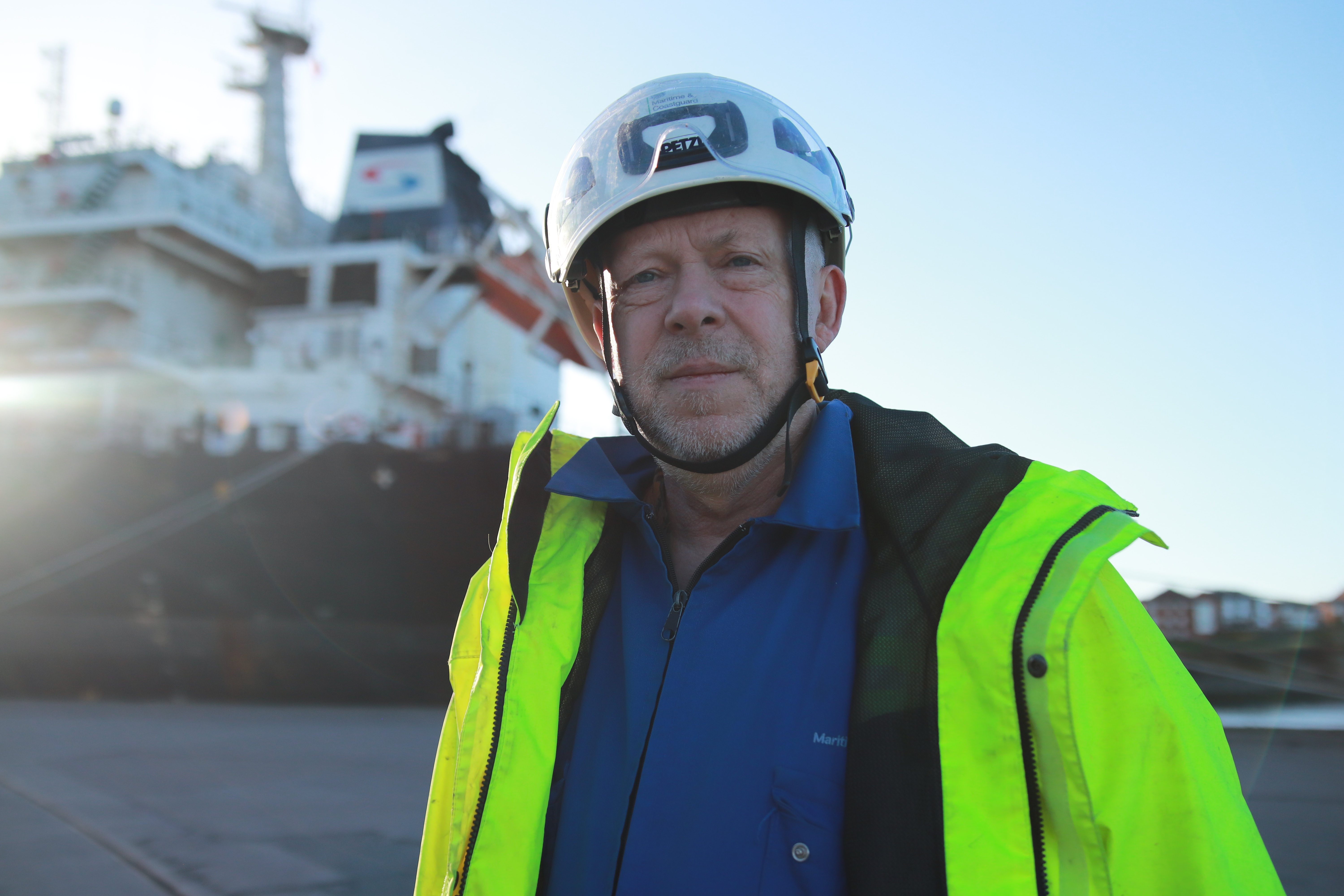 Chris Bates, a Surveyor, stands on the dock with a large vessel in the background