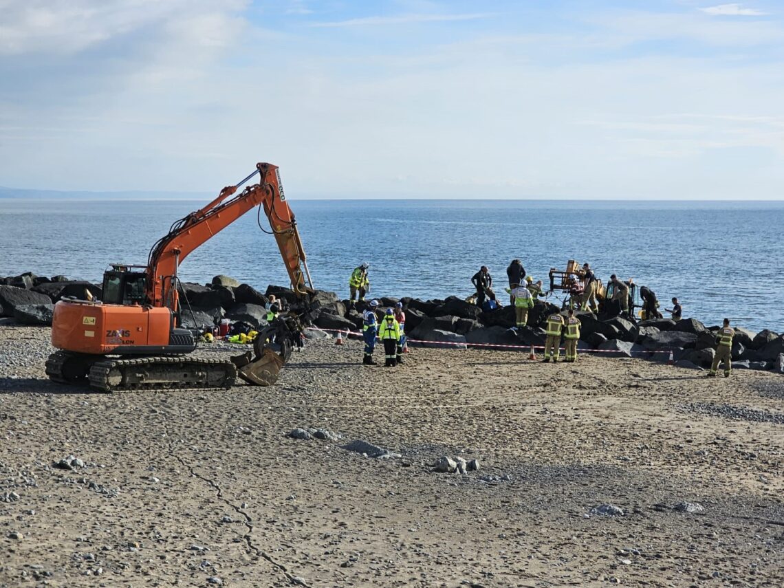 Emergency services work at the Tywyn beach rock armour with an excavator nearby