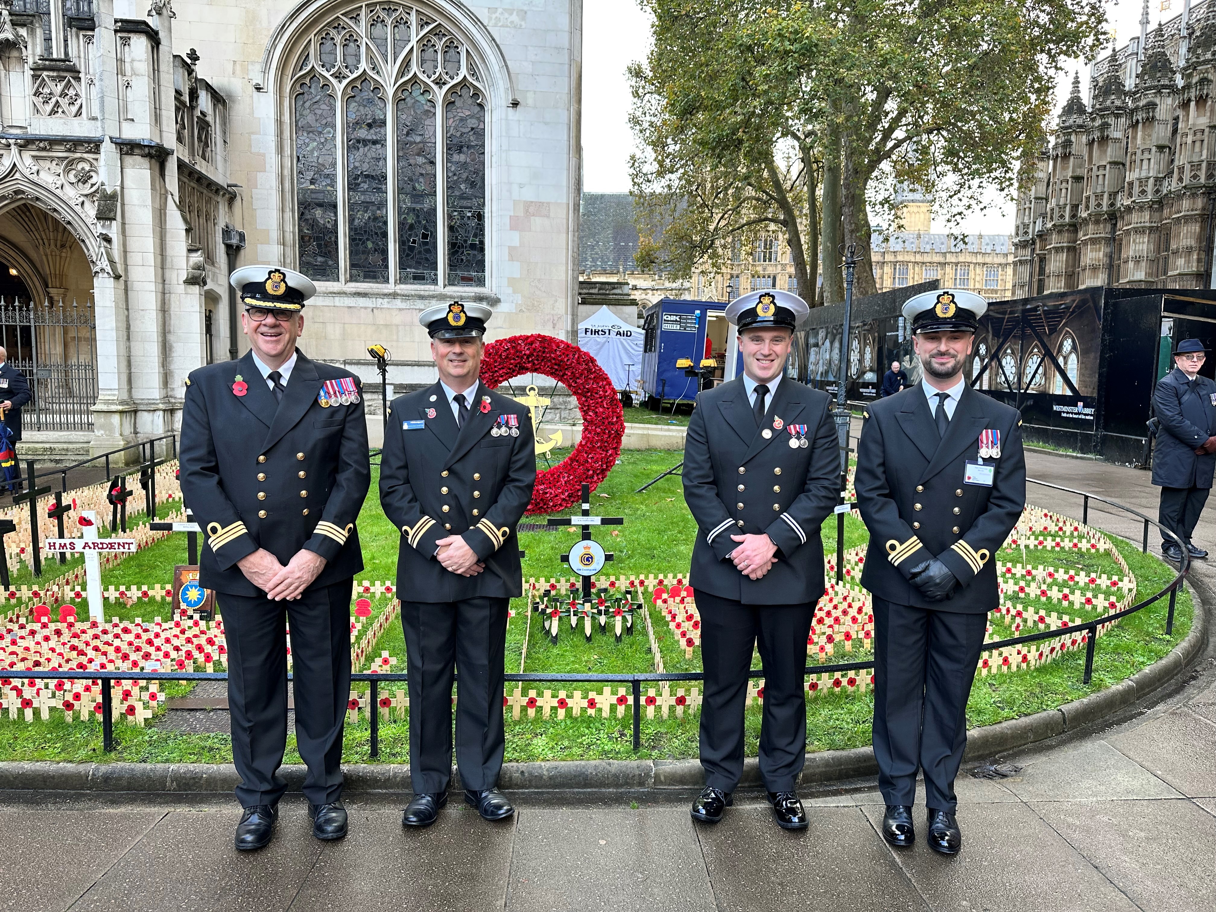 Four men in HM Coastguard dress uniform stood in front of coastguard poppy plot