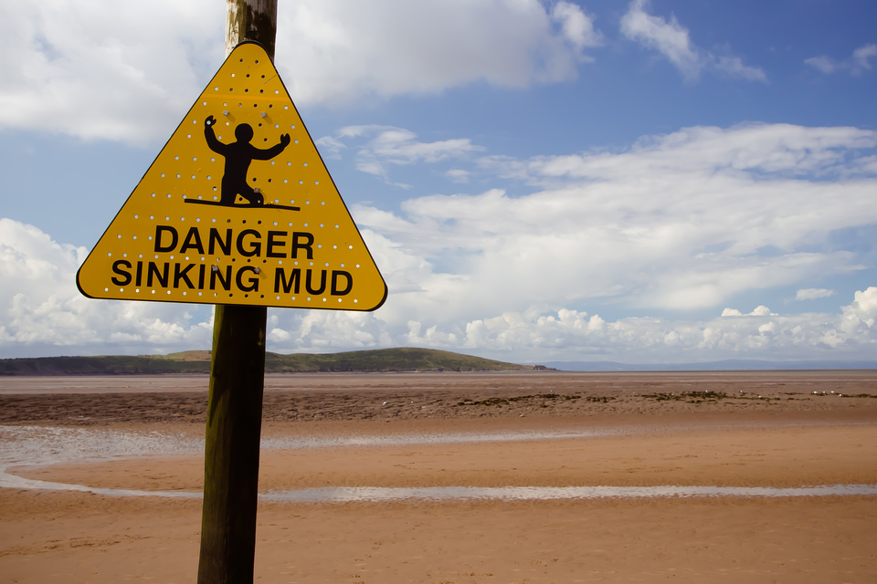 A sign by the beach warning of sinking mud