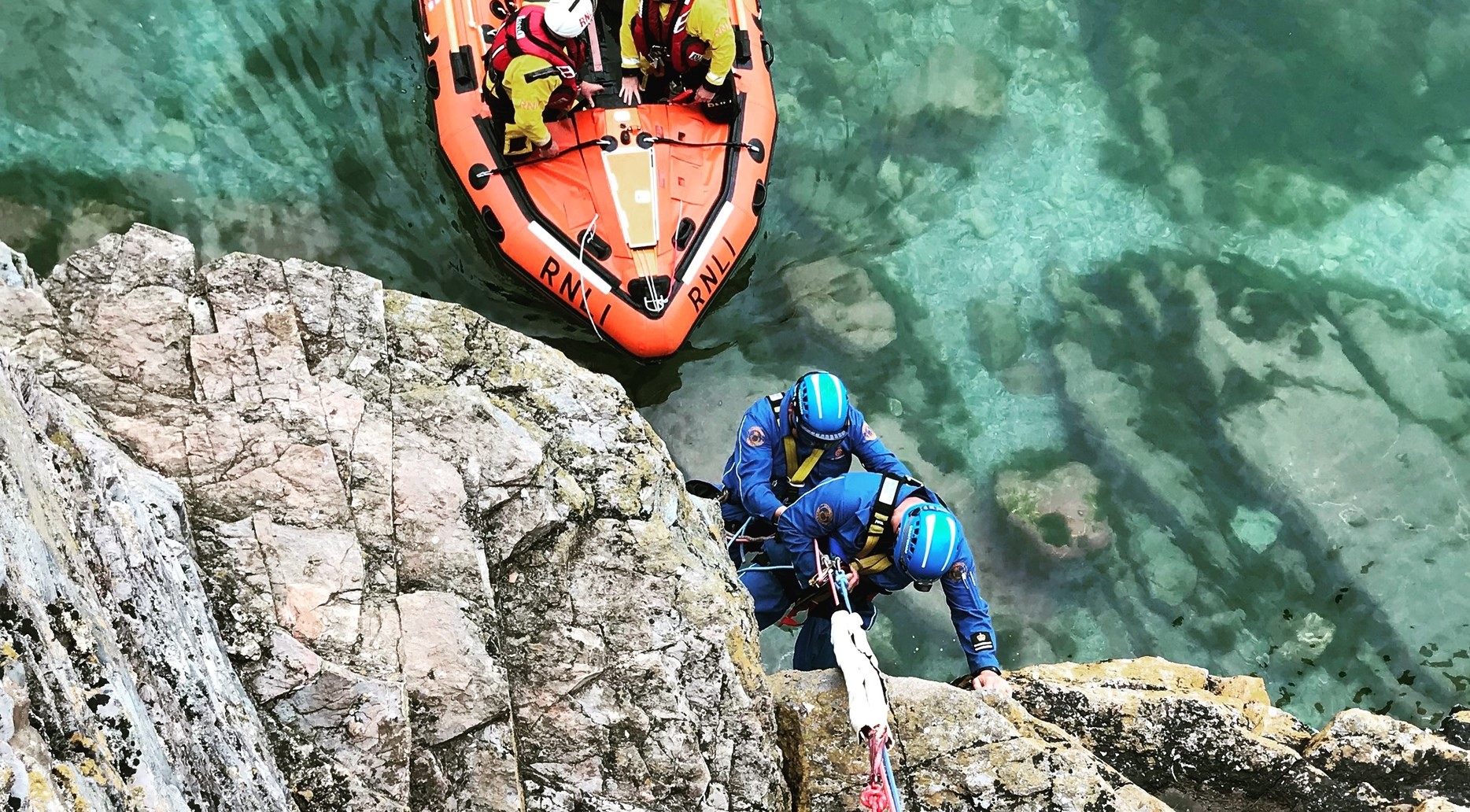 An RNLI lifeboat below HM Coastguard rope rescue team on a cliff