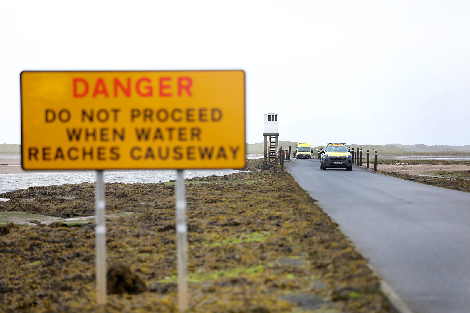 Warning sign on causeway of Holy Island with HM Coastguard vehicle in background