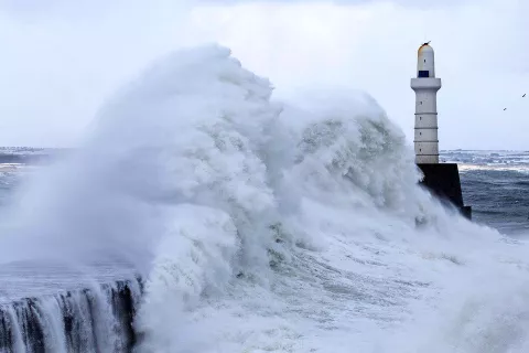 Waves crashing on the coast in front of a lighthouse