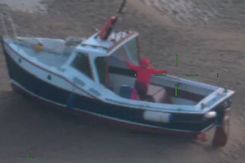 Woman stands on moored boat on Blakeney Point, Norfolk. Image is slightly blurry as it taken from the fixed wing aircraft, nearly 1,200 feet above the boat.