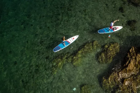 Aerial shot of two stand up paddleboarders near rocks.