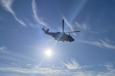 Coastguard helicopter and winch paramedic on the wire over cliff with blue sea and sky