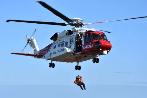 A winch paramedic hangs by a wire from an HM Coastguard search and rescue helicopter