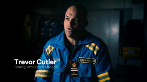 Screenshot from TV series of Coastguard officer in uniform sat in front of a darkened background