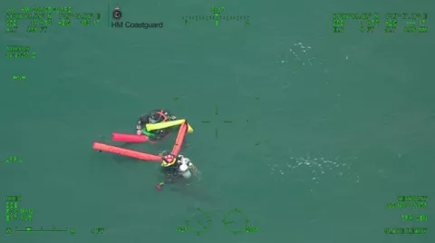 Two divers with high visibility floats in open water, seen through helicopter camera