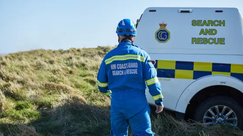A coastguard rescue officer stands by an HM Coastguard van by a cliff