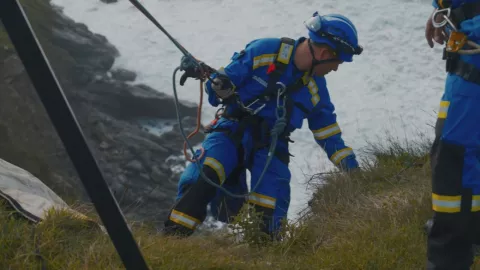 A Coastguard Rescue Officer rope technician carefully goes down over a cliff edge, attached to a rope