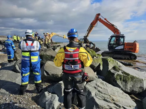 Coastguard officers observe as an excavator operates by rock armour at Tywyn beach