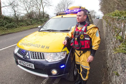 Senior Coastal Operations Officer Ryan Gray in safety kit standing next to an HM Coastguard vehicle