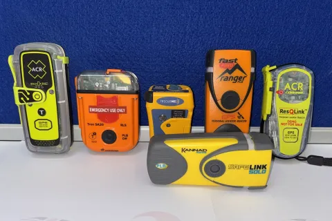 Six different makes of PLB, with colours of bright orange and yellow, are lined up against a blue background