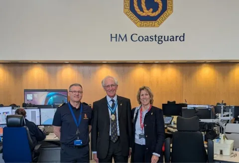 In the JRCC operations room with an HM Coastguard logo behind them stand Matt West, William Maltby and Sarah Maltby