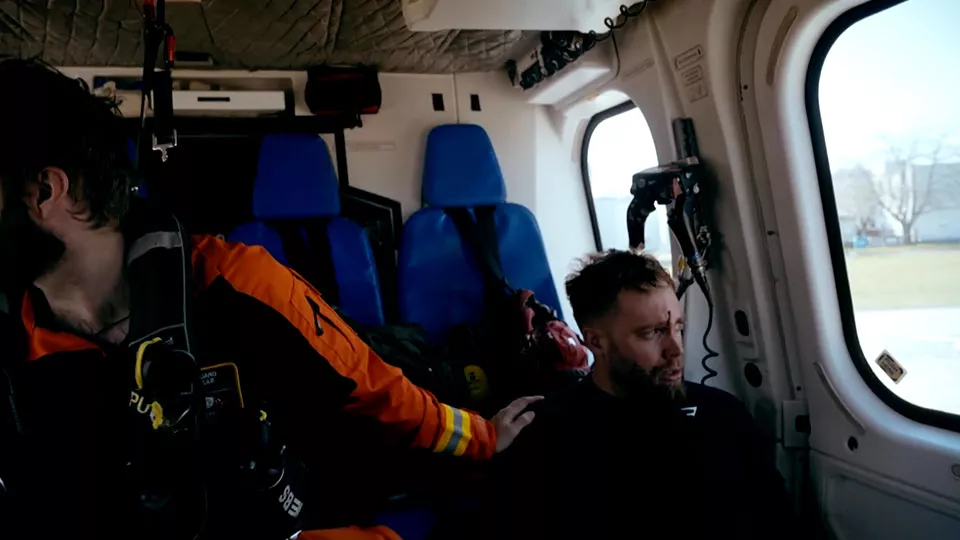 A man in a helicopter sits next to the helicopter crew after being rescued