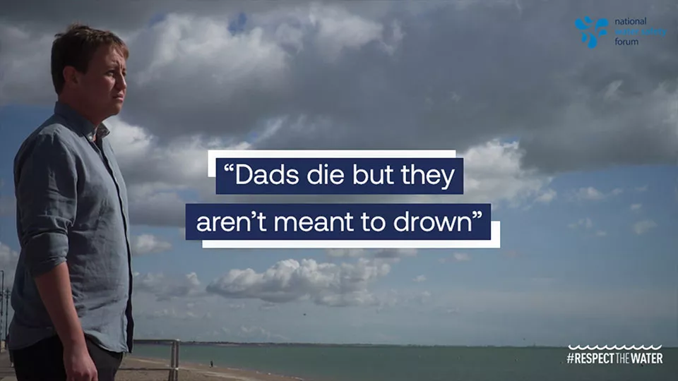 A man stands to the left of the image looking out to sea. A quote with white text on a blue background reads "dads die but they aren't meant to drown" in the middle of the photo.