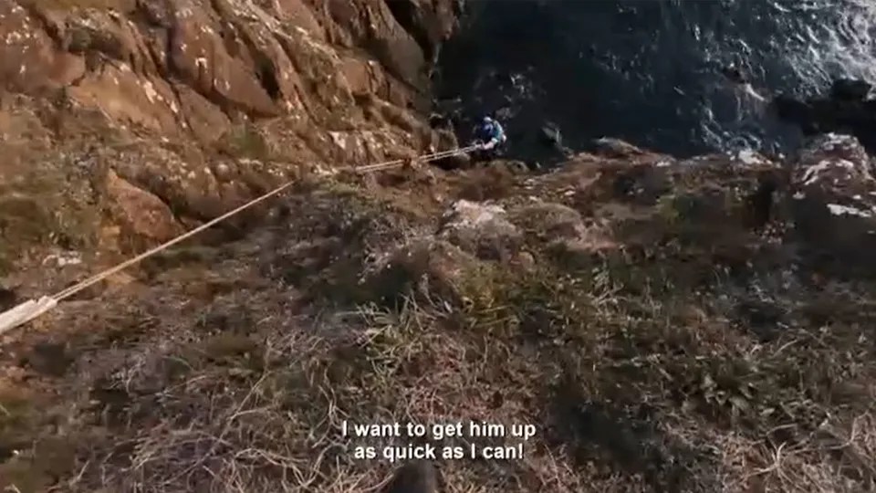 The view of a cliff rescue looking down a cliff towards a coastguard rescue officer