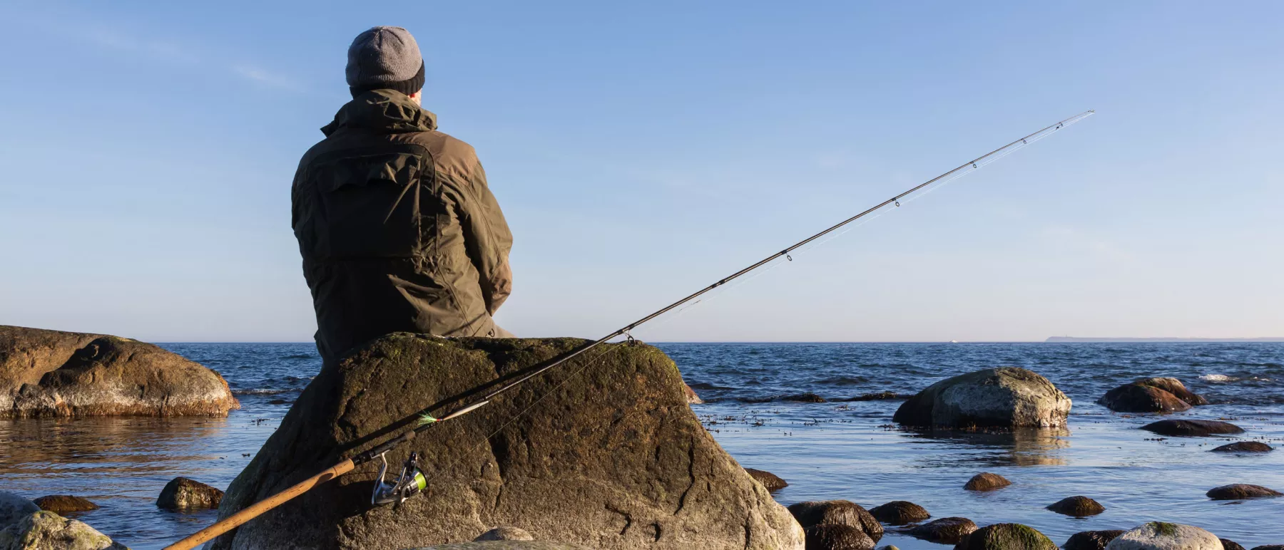 Angler sat with their fishing rod on rocks close to the water