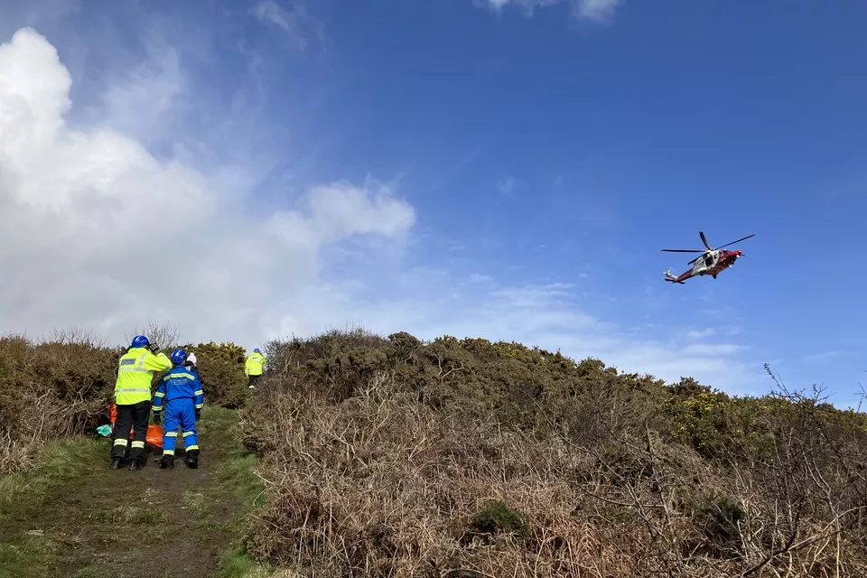 Coastguard helicopter hovers over team and casualty awaiting air lift