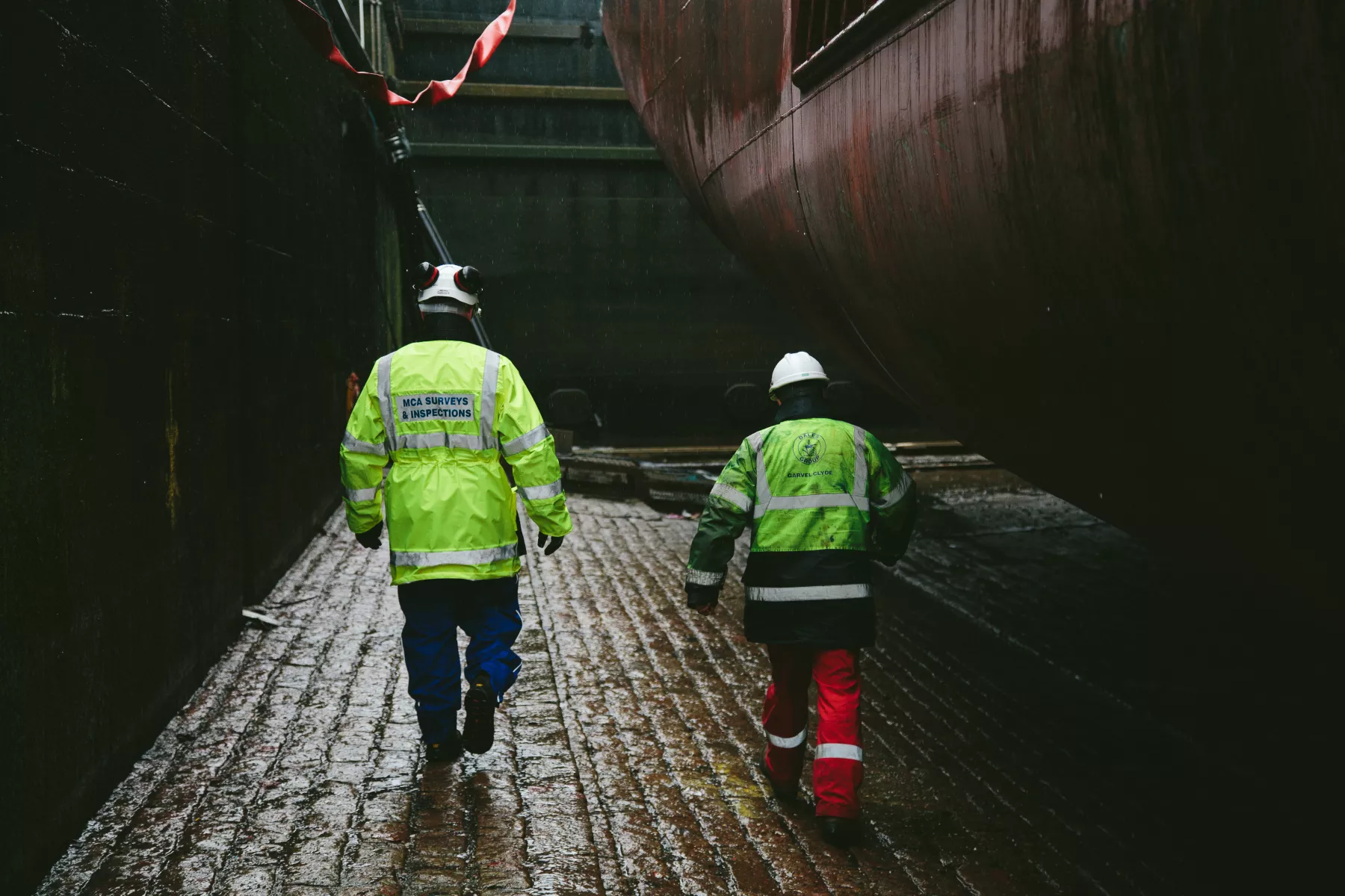 Two surveyors in high-vis walking underneath dry docked vessel during inspection