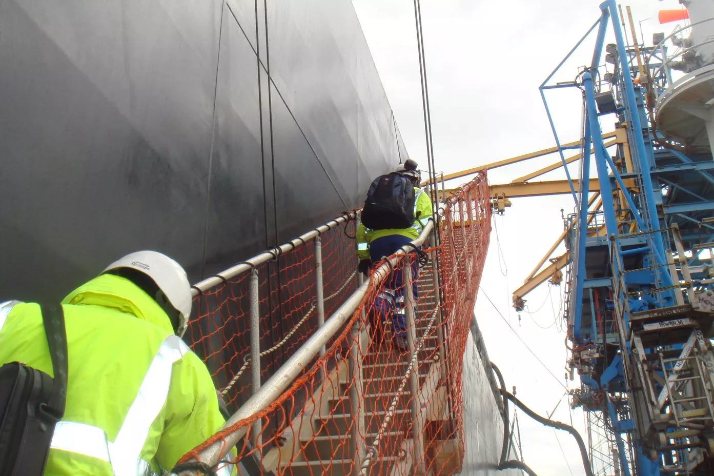 Two people in high-vis climbing a gangway onto a large vessel