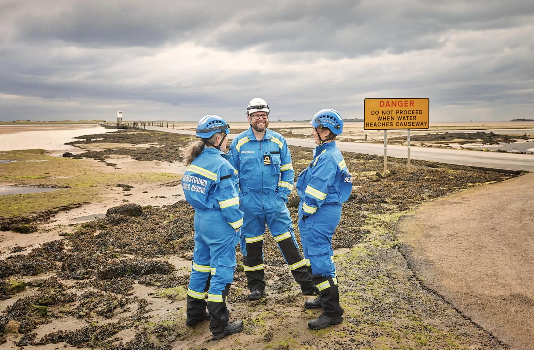 Three Coastguards stood facing each other, smiling, at Holy Island Causeway