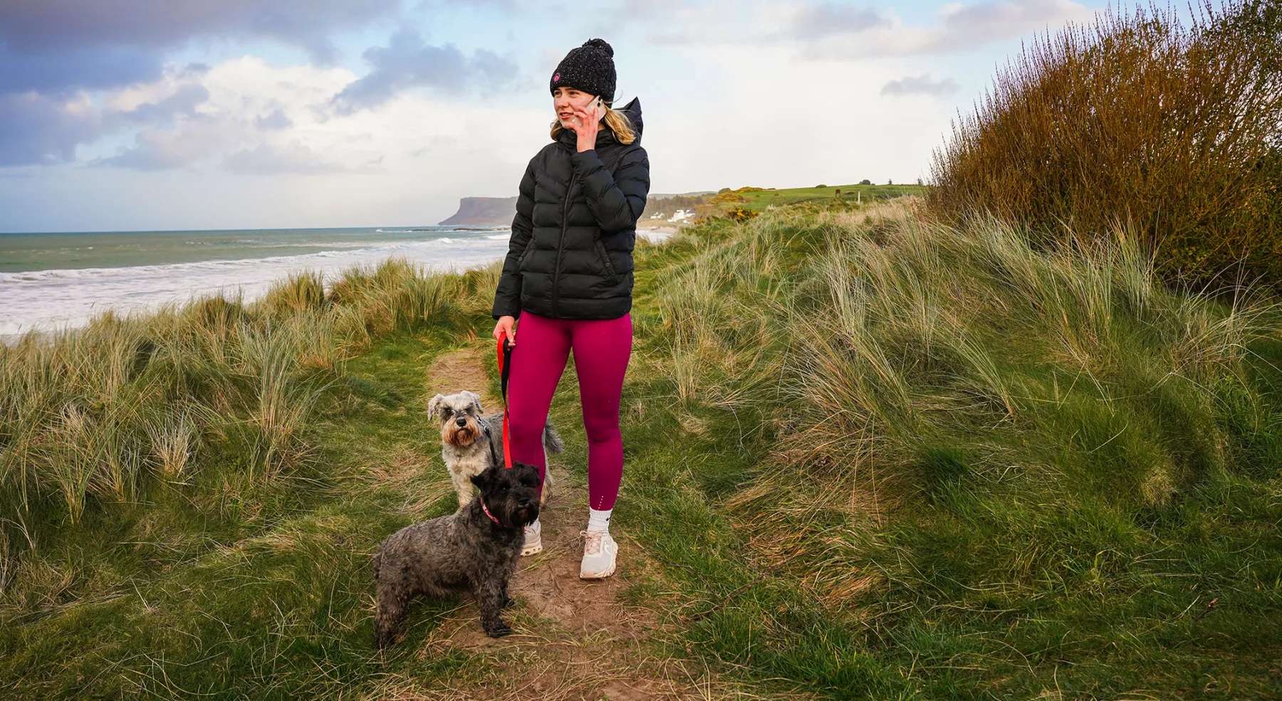 Young woman on phone while walking dogs along the coast