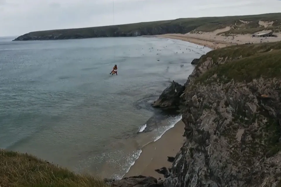 The view of the cliffs of Holywell Bay and a person being winched into the air