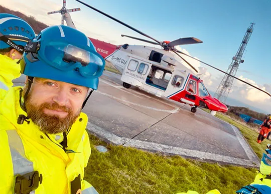 A male senior coastal operations officer stands in front of a helicopter