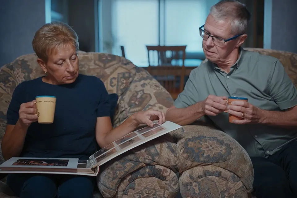 A man and a woman sit on a sofa looking through a photo album