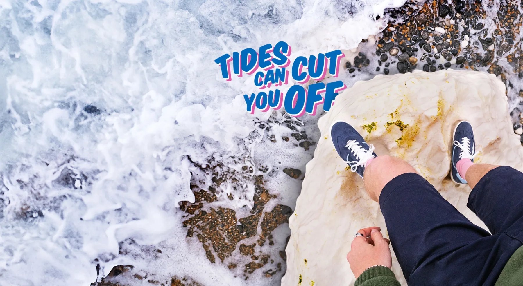 A point of view shot looking down onto the ground. Two feet are stood on a rock surrounded by the incoming tide
