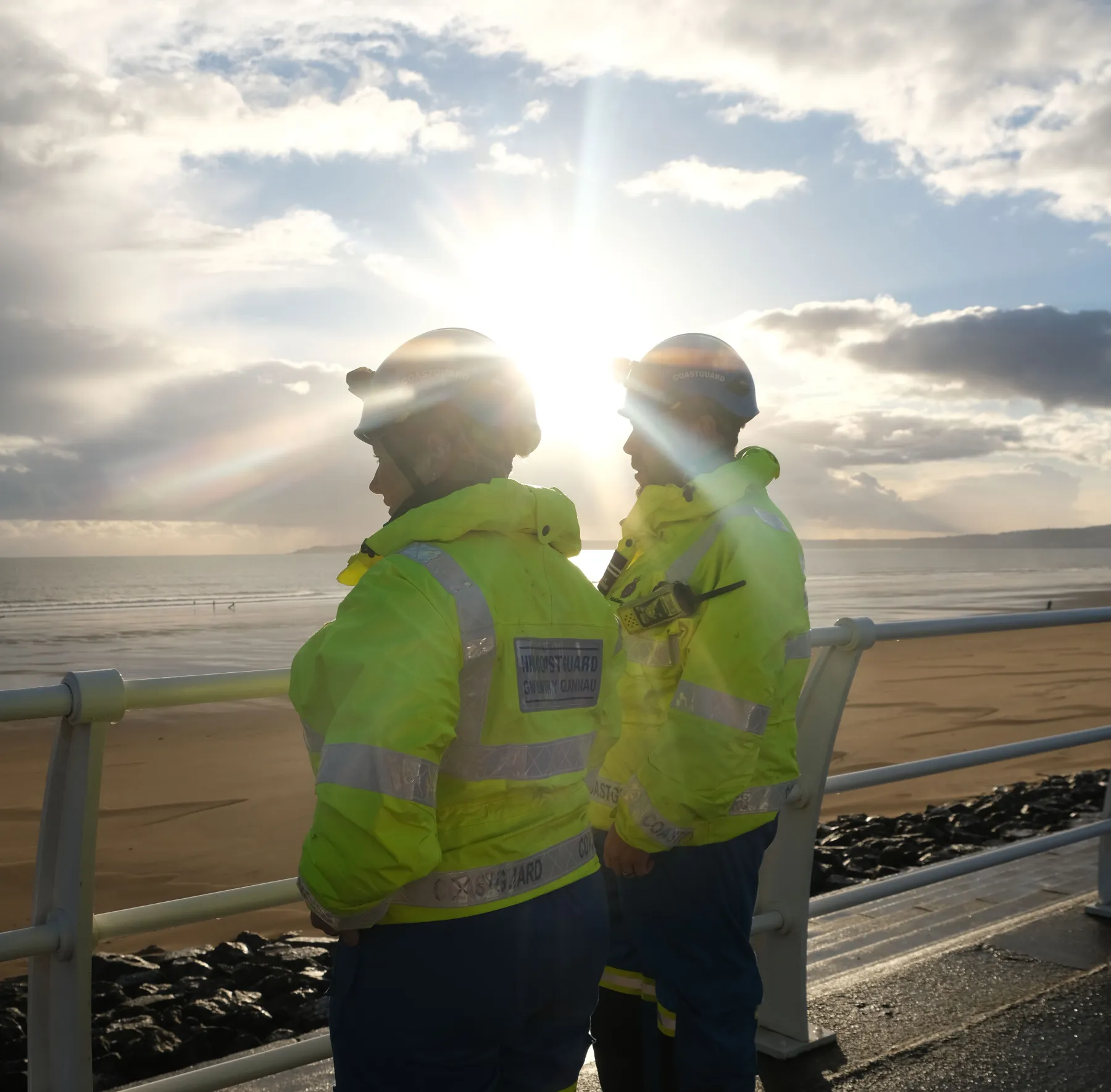 Two coastguard rescue officers on a promenade in Wales look out across the bay