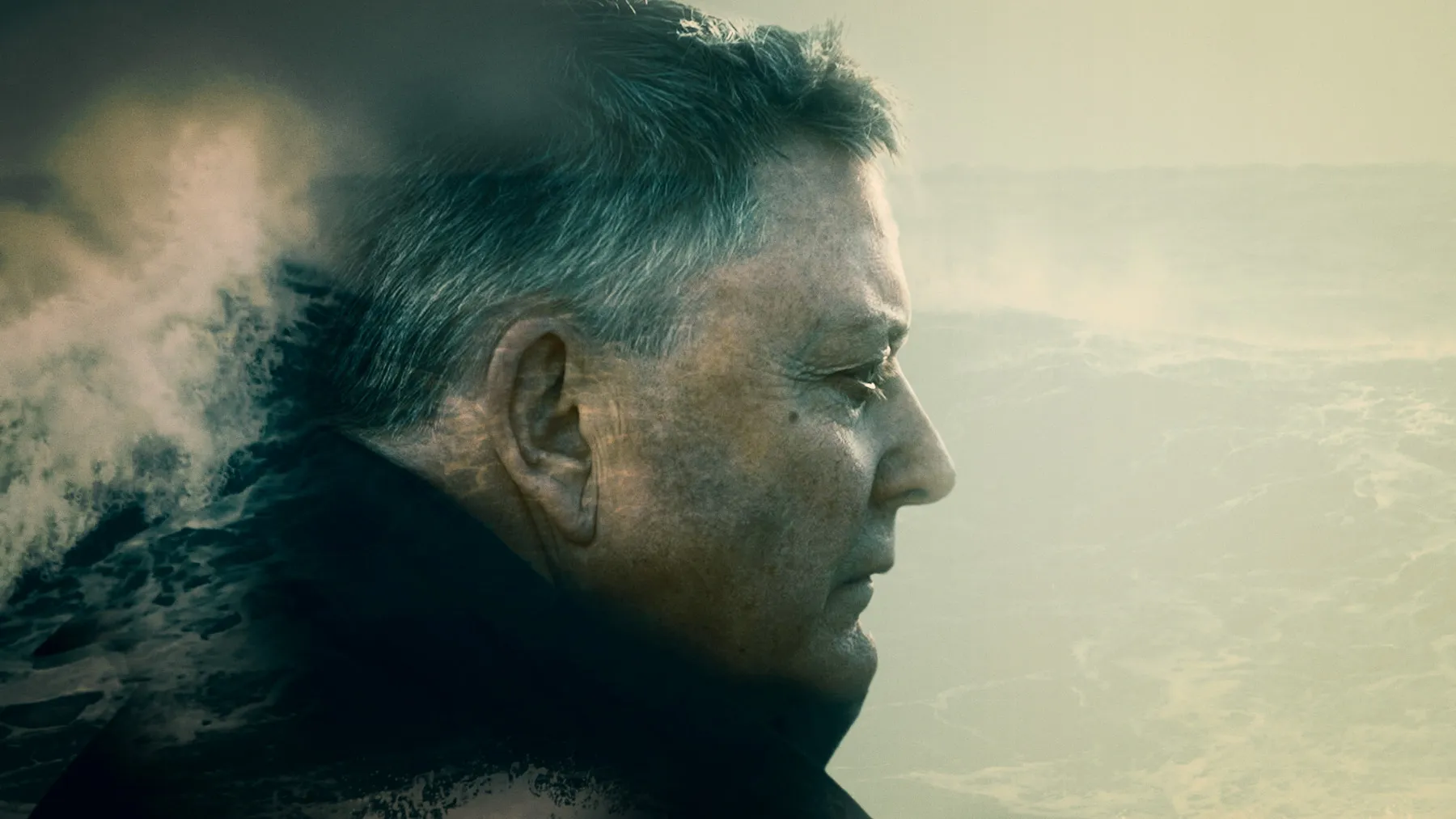 A man stands against a moody grey sky. Crashing waves are overlaid over the top to form a dramatic image.