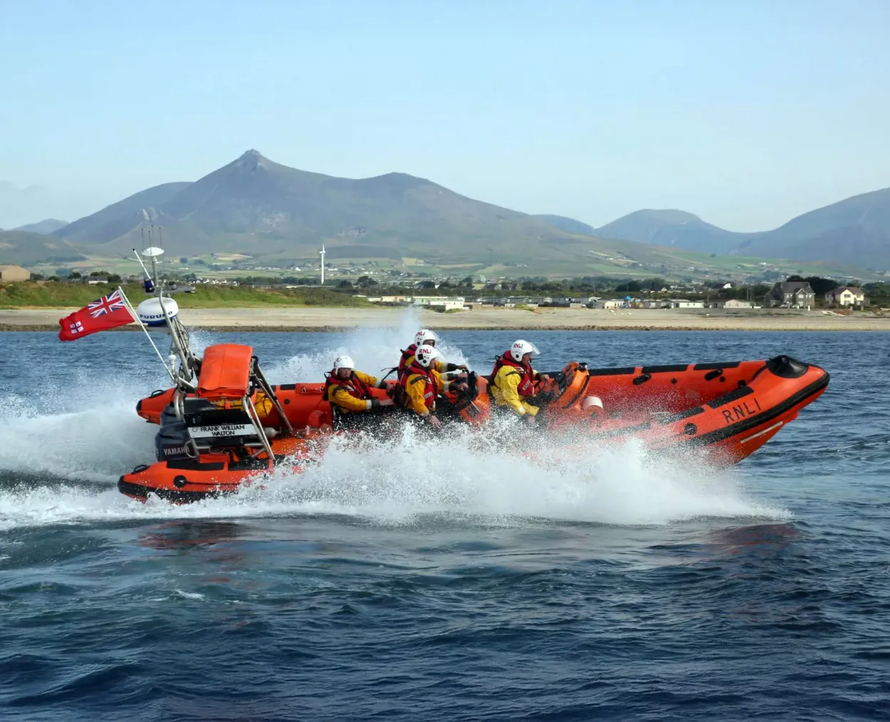 orange lifeboat speeding through the water with mountains in the distance