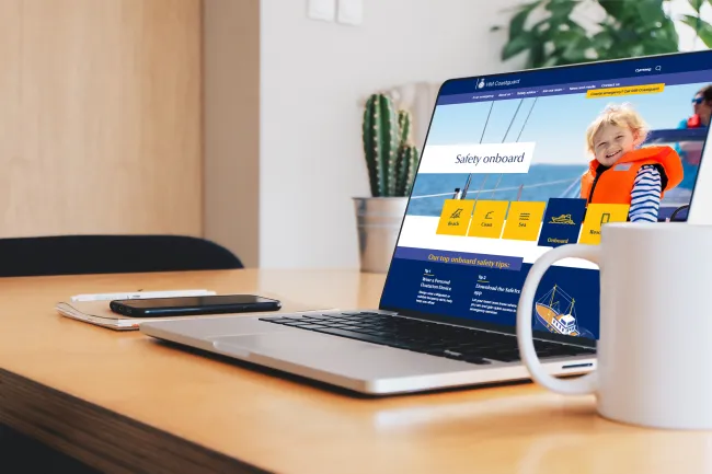 A page from the HM Coastguard website presented on a laptop on a desk next to a mug of coffee