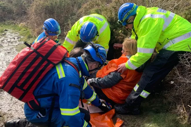 Members of the Llansteffan Coastguard Rescue Team wearing bright hi-vis jackets and blue helmets attend to the casuality on the ground