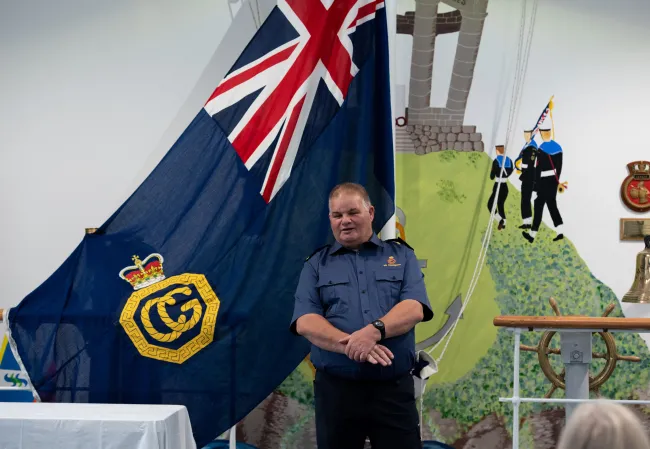 Colin Moir stands in front of a HMN Coastguard flag at his retirement presentation