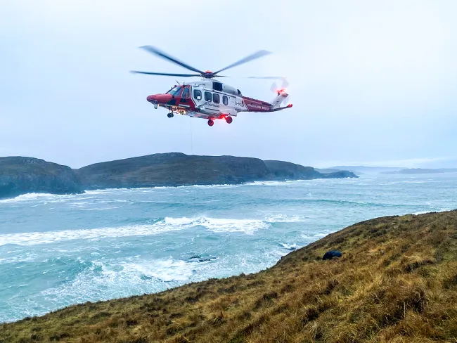 The R151 HM Coastguard Rescue Helicopter lifts a stranded surfer from rocks at Farr Bay, Scotland. 