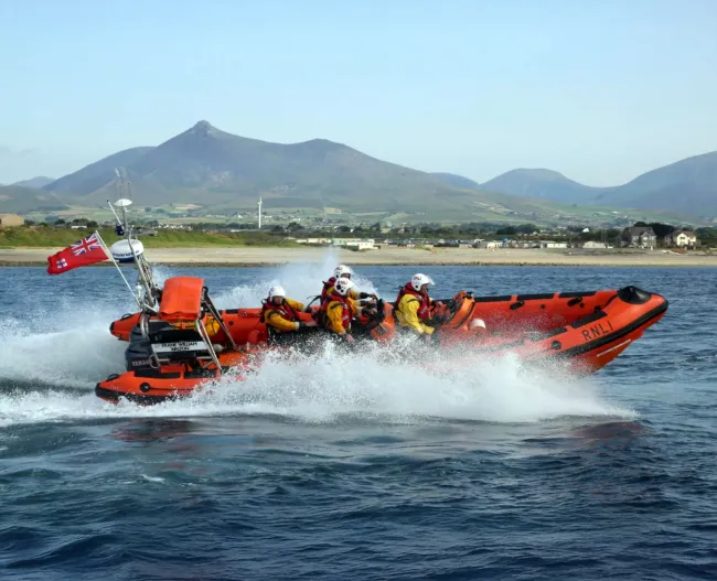 orange lifeboat speeding through the water with mountains in the distance