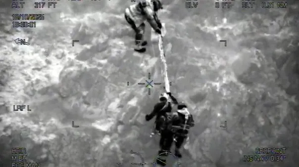Night-vision image of a climber on a rope being helped up the cliff by two Coastguard Rescue Officers