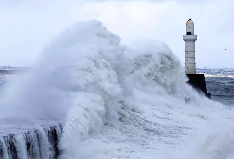 Waves crashing on the coast in front of a lighthouse