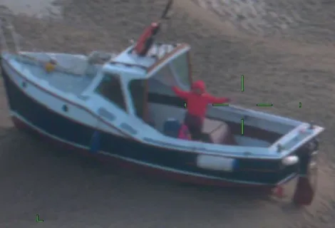 Woman stands on moored boat on Blakeney Point, Norfolk. Image is slightly blurry as it taken from the fixed wing aircraft, nearly 1,200 feet above the boat.