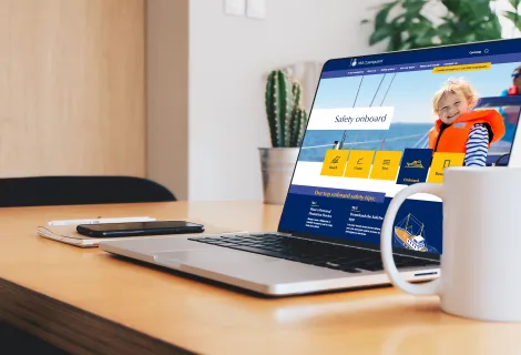 A page from the HM Coastguard website presented on a laptop on a desk next to a mug of coffee