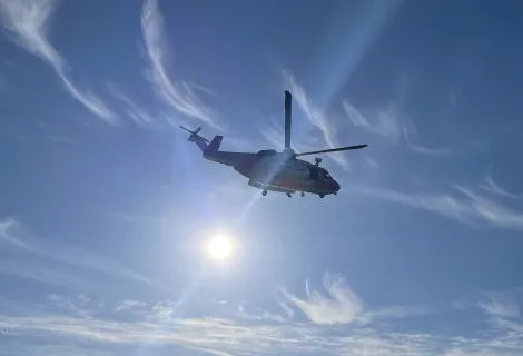 Coastguard helicopter and winch paramedic on the wire over cliff with blue sea and sky