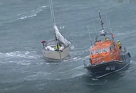 White sailing yacht and orange and blue RNLI vessel in stormy waters