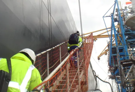 Two people in high-vis climbing a gangway onto a large vessel