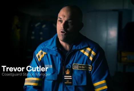 Screenshot from TV series of Coastguard officer in uniform sat in front of a darkened background